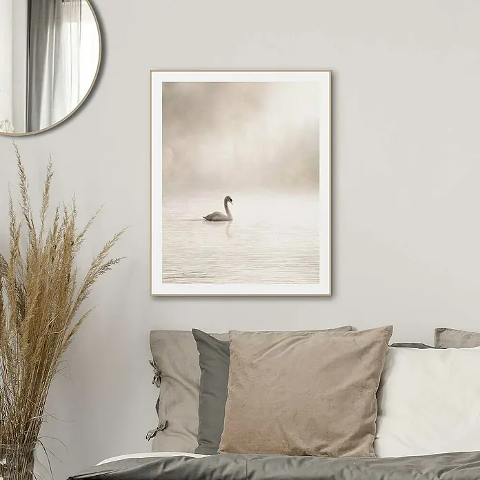 Reinders Bild Slim Frame Wood - Misty Lake Swan, B x H: 40 x 50 cm - Ein gerahmtes Kunstwerk mit einem Schwan, der friedlich auf einem ruhigen See schwimmt, hängt über einem stilvollen Bett mit Kissen.