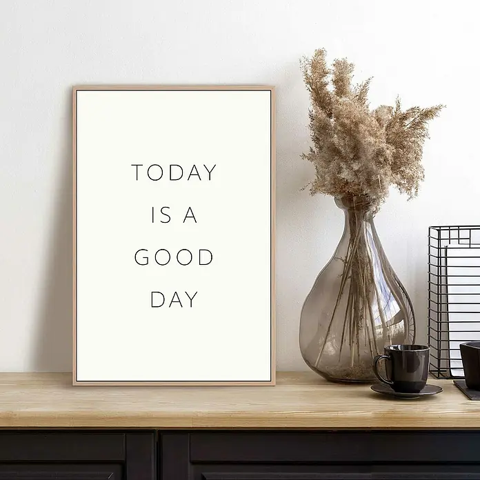 Reinders Bild Slim Frame Wood - Today, B x H: 20 x 30 cm - Ein gerahmtes Poster mit der Aufschrift "Heute ist ein guter Tag" steht auf einem Tisch neben einer Vase mit Trockenblumen und einer Tasse.