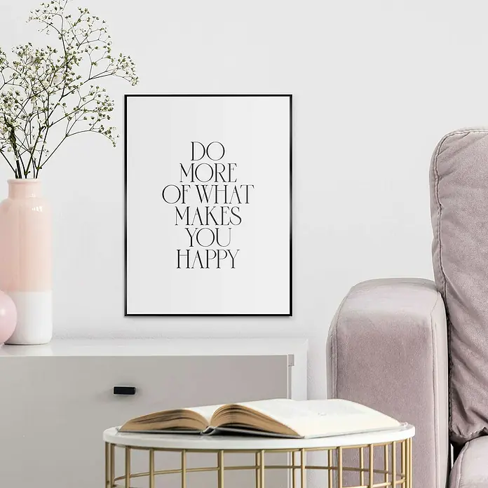 Reinders Bild Slim Frame Black - More Happiness, B x H: 30 x 40 cm - Ein gerahmtes, inspirierendes Wandbild mit dem Schriftzug "Do More of What Makes You Happy" hängt über einem modernen Beistelltisch.