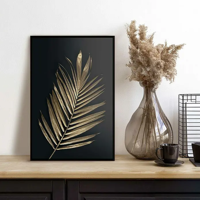 Reinders Bild Slim Frame Black - Areca Palmenblatt, B x H: 20 x 30 cm - Nahaufnahme eines gerahmten Bildes eines goldenen Palmenblattes auf schwarzem Hintergrund, neben einer Vase und Tasse auf einem Tisch.