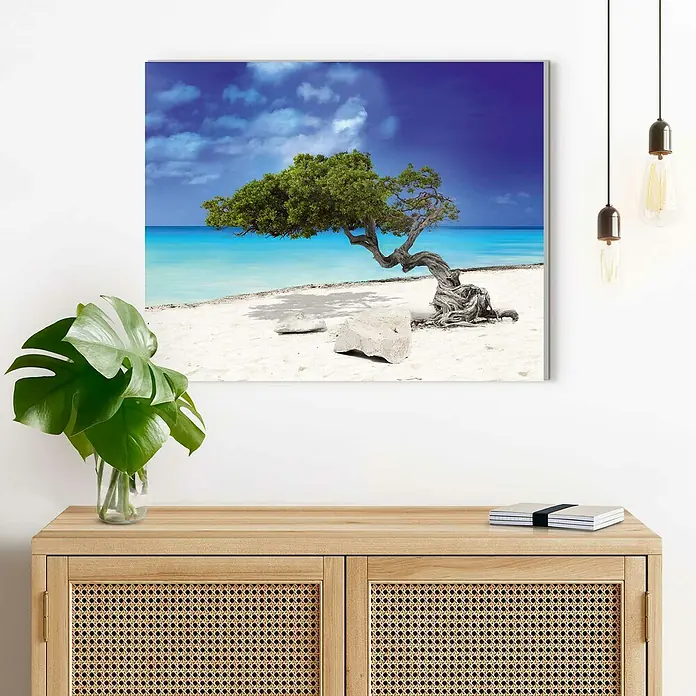 Reinders Decopanel - Tropical Tree, B x H: 50 x 40 cm - Ein gerahmtes Wandbild mit einem markanten Divi-Divi-Baum am Strand, das über einem hellen Holzschrank mit Rattan-Details hängt.