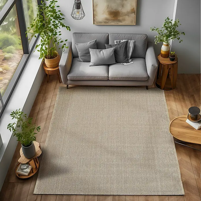 Flachgewebeteppich Loom - Beige, 340 x 240 cm, 100 % Polypropylen - Ein beigefarbener Teppich liegt in einem Wohnzimmer mit einem grauen Sofa, Pflanzen und Holzböden. Der Teppich verleiht dem Raum Wärme und Textur.