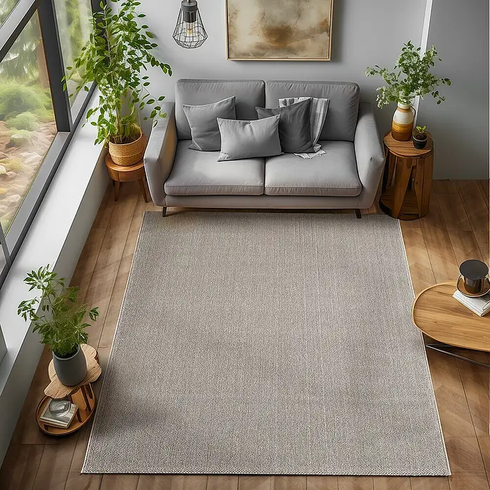 Flachgewebeteppich Loom - Braun, 200 x 140 cm, 100 % Polypropylen - Ein hellgrauer Teppich liegt in einem Wohnzimmer mit einem grauen Sofa, Pflanzen und Holzböden.
