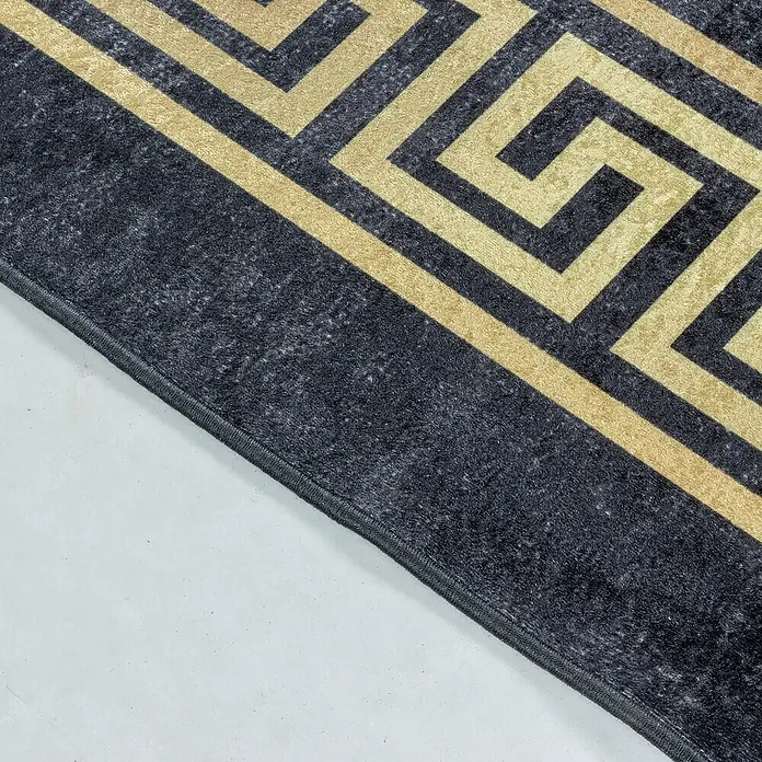 Flachgewebeteppich Fiesta - Schwarz/Gold, 150 x 80 cm, 100 % Polyester - Nahaufnahme eines Teppichs mit einem geometrischen, griechisch inspirierten Muster in Gold und Dunkelgrau, der auf einem hellen Untergrund liegt.