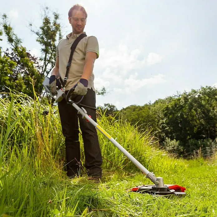 AL-KO Elektro-Motorsense BC 1200 E - 1.200 W - Ein Mann benutzt einen Rasentrimmer, um hohes Gras in einem Garten zu schneiden. Der Trimmer hat einen roten Schutz und einen langen Schaft.