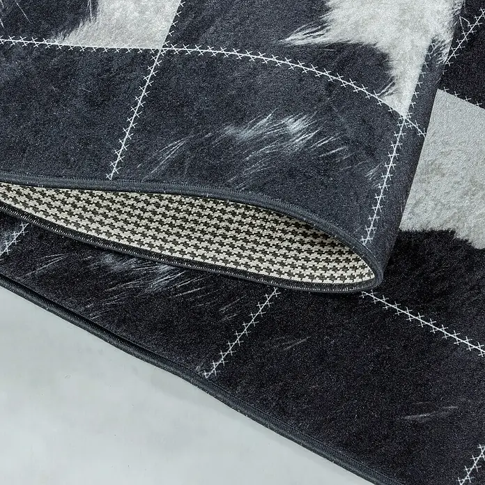 Flachgewebeteppich Fiesta - Schwarz/Weiß, 290 x 200 cm, 100 % Polyester - Detailaufnahme eines schwarz-grauen Teppichs mit Karomuster und dekorativen Ziernähten. Die Unterseite zeigt ein feines Fischgrätmuster.