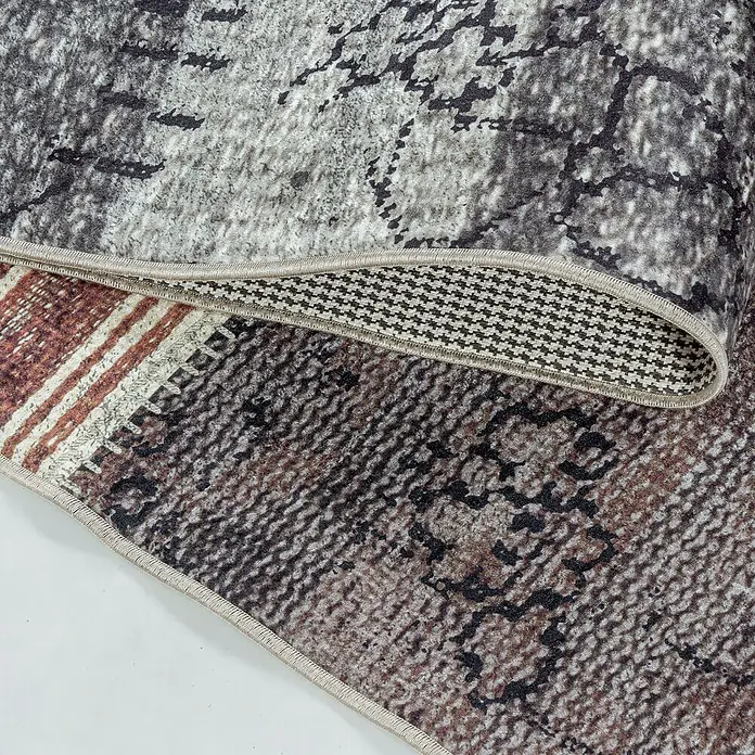 Flachgewebeteppich Fiesta - Multi, 250 x 80 cm, 100 % Polyester - Nahaufnahme eines Teppichs mit abstraktem Muster und aufgerolltem Rand, der die Unterseite mit einem Fischgrätenmuster zeigt.