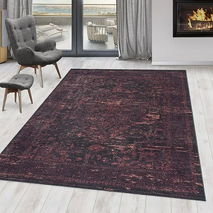 Flachgewebeteppich Fiesta - Rot, 230 x 160 cm, 100 % Polyester - Ein stilvoller, gemusterter Teppich in dunklen Farbtönen liegt in einem hellen Raum mit Sessel und Kamin.
