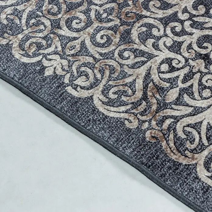 Flachgewebeteppich Fiesta - Schwarz, 150 x 80 cm, 100 % Polyester - Detailaufnahme eines Teppichs mit grauem, floralem Muster und einem dunklen Rand auf hellem Untergrund.