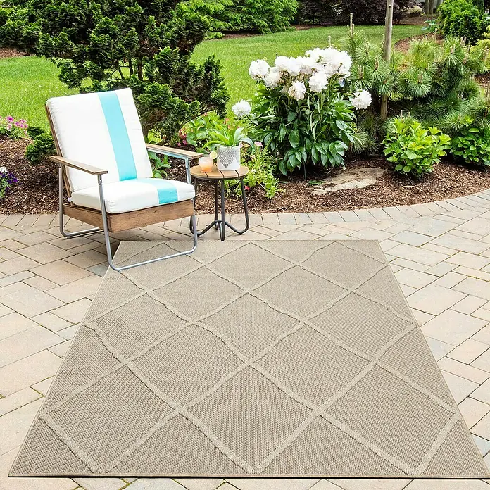 Outdoor-Teppich Patara VI - Beige, 230 x 160 cm, 100 % Polypropylen - Ein beiger Outdoor-Teppich mit einem geometrischen Rautenmuster liegt auf einer Terrasse neben einem Stuhl und einem Beistelltisch.