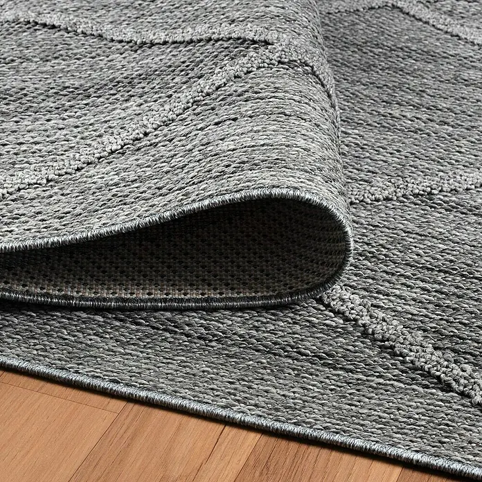 Outdoor-Teppich Patara VI - Grau, 250 x 80 cm, 100 % Polypropylen - Nahaufnahme eines grauen Teppichs mit geometrischem Muster, der teilweise aufgerollt ist und die Textur und Verarbeitung betont.