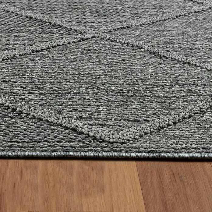 Outdoor-Teppich Patara II - Grau, 250 x 80 cm, 100 % Polypropylen - Detailaufnahme eines grauen Teppichs mit geometrischem Muster, der auf einem Holzboden liegt. Der Teppich hat eine markante Textur.