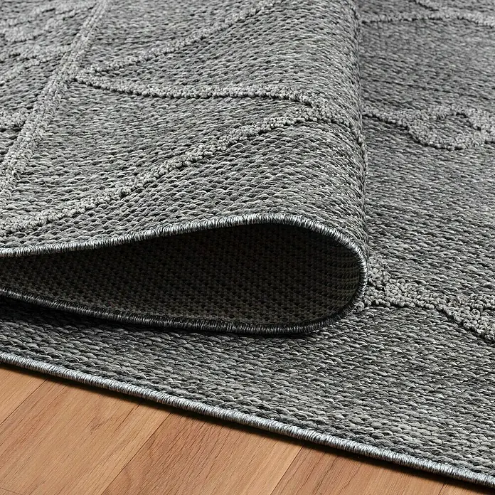 Outdoor-Teppich Patara II - Grau, 250 x 80 cm, 100 % Polypropylen - Grauer Teppich mit geometrischem Muster teilweise aufgerollt auf einem Holzboden, der seine Textur und Verarbeitung hervorhebt.