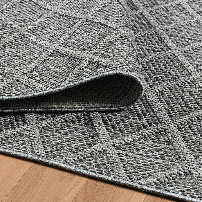 Outdoor-Teppich Patara V - Grau, 250 x 80 cm, 100 % Polypropylen - Ein grauer Teppich mit geometrischem Muster liegt auf einem Holzboden und ist an einer Ecke aufgerollt, um die Unterseite zu zeigen.