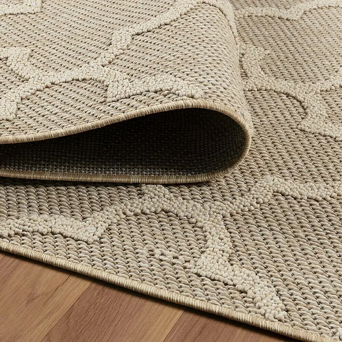 Outdoor-Teppich Patara IV - Beige, 340 x 240 cm, 100 % Polypropylen - Nahaufnahme eines beigen Outdoor-Teppichs mit geometrischem Muster und aufgerolltem Rand, der seine Textur und Verarbeitung zeigt.