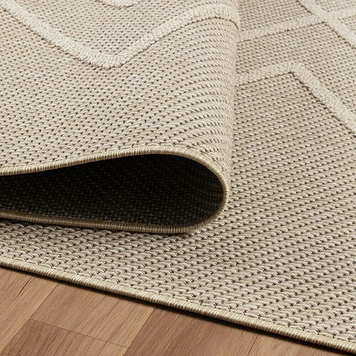 Outdoor-Teppich Patara I - Beige, 230 x 160 cm, 100 % Polypropylen - Nahaufnahme eines beigen Teppichs mit geometrischem Muster, dessen Ecke aufgerollt ist und die Textur hervorhebt.