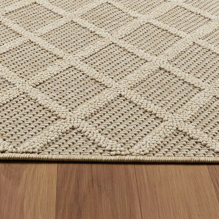 Outdoor-Teppich Patara V - Beige, 200 x 140 cm, 100 % Polypropylen - Nahaufnahme eines beigen Teppichs mit geometrischem Muster, der auf einem Holzboden liegt. Die Textur und das Design des Teppichs sind gut sichtbar.
