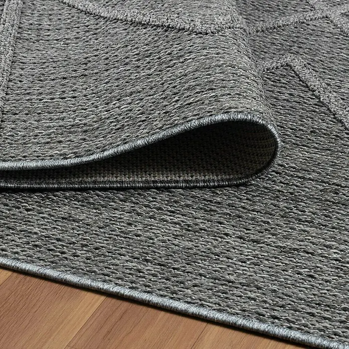 Outdoor-Teppich Patara I - Grau, 170 x 120 cm, 100 % Polypropylen - Nahaufnahme eines grauen Teppichs mit geometrischem Muster und gewebter Textur, der auf einem Holzboden liegt.