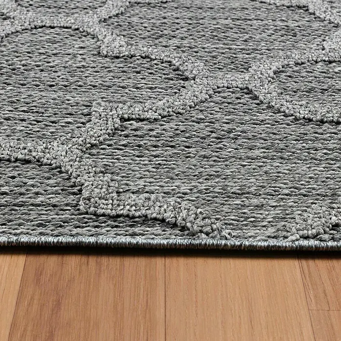 Outdoor-Teppich Patara IV - Grau, 200 x 140 cm, 100 % Polypropylen - Detailaufnahme eines grauen Teppichs mit geometrischem Muster auf einem Holzboden, das die Textur und das Design hervorhebt.