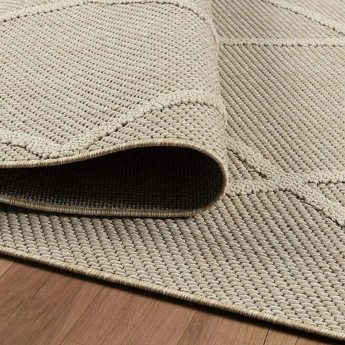 Outdoor-Teppich Patara VI - Beige, 230 x 160 cm, 100 % Polypropylen - Nahaufnahme eines hellbraunen Teppichs mit subtilen geometrischen Mustern, teilweise aufgerollt, um die Textur zu zeigen.