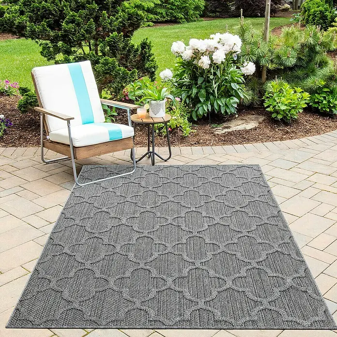 Outdoor-Teppich Patara IV - Grau, 200 x 140 cm, 100 % Polypropylen - Ein grauer Outdoor-Teppich mit marokkanischem Muster liegt auf einer Terrasse neben einem Stuhl und einem Beistelltisch.