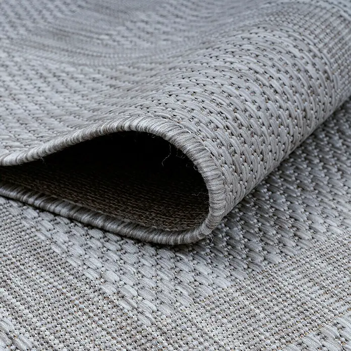 Outdoor-Teppich Relax - Silber, Durchmesser: 120 cm, 100 % Polypropylen - Nahaufnahme eines grauen Teppichs mit aufgerollter Ecke, der seine Textur und Verarbeitung zeigt. Perfekt für jeden Raum, robust und stilvoll.