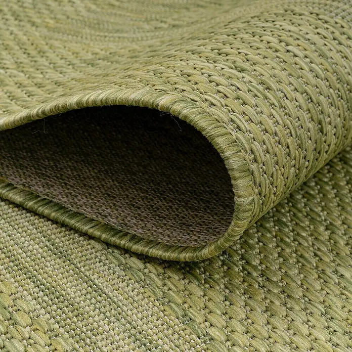 Outdoor-Teppich Relax - Grün, 230 x 160 cm, 100 % Polypropylen - Detailaufnahme eines gewebten grünen Teppichs, der teilweise eingerollt ist, wodurch seine Textur und Verarbeitung hervorgehoben werden.