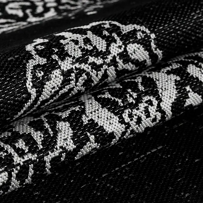 Outdoor-Teppich Sunny VIII - Schwarz, 170 x 120 cm, 100 % Polypropylen - Nahaufnahme eines gewebten Teppichs mit einem komplizierten, kontrastreichen Muster aus Schwarz und Weiß.