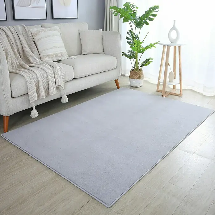 Kurzflorteppich SkySilber, 340 x 240 cm, 100 % Polyester - Ein weicher, grauer Teppich liegt vor einem Sofa und einem Beistelltisch mit Dekoration, der den Raum gemütlich wirken lässt.