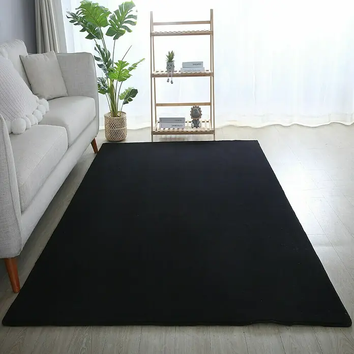 Kurzflorteppich Sky - Schwarz, 230 x 160 cm, 100 % Polyester - Einrichtungsszene mit einem großen, schwarzen Teppich, der den Raum dominiert, ergänzt durch ein graues Sofa und ein Holzregal.