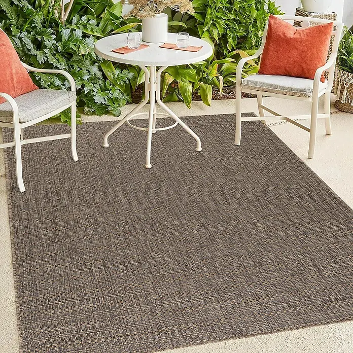 Outdoor-Teppich Zagora III - Kupfer, 150 x 80 cm, 100 % Polypropylen - Ein brauner Outdoor-Teppich liegt auf einer Terrasse mit Gartenmöbeln, die eine einladende Atmosphäre schaffen.