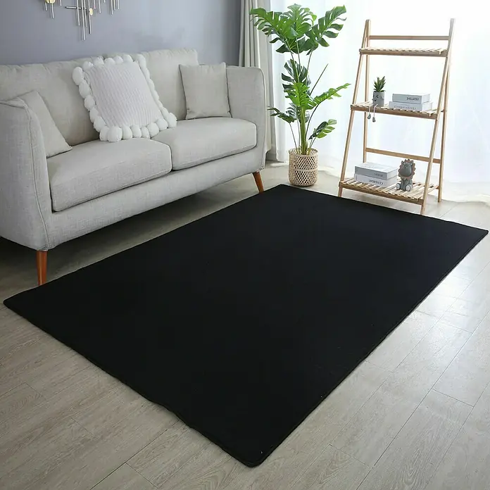 Kurzflorteppich Sky - Schwarz, 230 x 160 cm, 100 % Polyester - Schwarzer Teppich im Wohnzimmer vor einem Sofa und einem Regal.