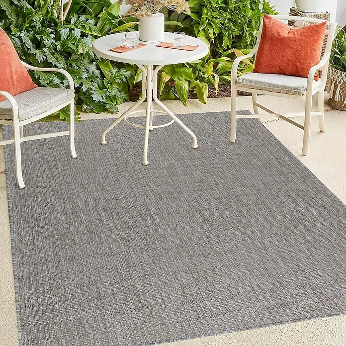 Outdoor-Teppich Zagora III - Beige, 170 x 120 cm, 100 % Polypropylen - Ein grauer Outdoor-Teppich liegt auf einer Terrasse mit Möbeln, der sich perfekt für den Außenbereich eignet und Stil verleiht.