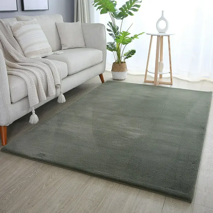 Hochflorteppich Pouffy - Grün, 170 x 120 cm, 100 % Polyester - Grauer Teppich im Wohnzimmer. Der Teppich liegt vor einem Sofa und einem Beistelltisch mit Dekorationen.