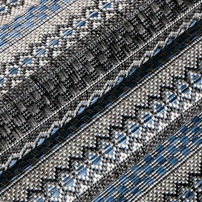 Outdoor-Teppich Sunny V - Schwarz, 170 x 120 cm, 100 % Polypropylen - Nahaufnahme eines gefalteten Stoffes mit einem komplexen blauen, grauen und schwarzen Webmuster, das Textur und Tiefe zeigt.