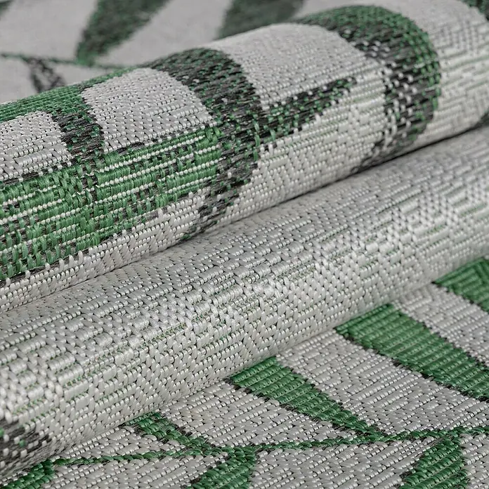 Outdoor-Teppich Sunny II - Grün, 170 x 120 cm, 100 % Polypropylen - Nahaufnahme eines gerollten Teppichs mit einem geometrischen Muster in Grün- und Grautönen, der eine strukturierte Oberfläche zeigt.