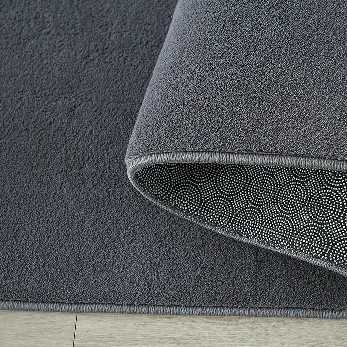 Kurzflorteppich Sky - Grau, 290 x 200 cm, 100 % Polyester - Detailaufnahme eines grauen Teppichs, der die Textur und die rutschfeste Unterseite hervorhebt.\n
