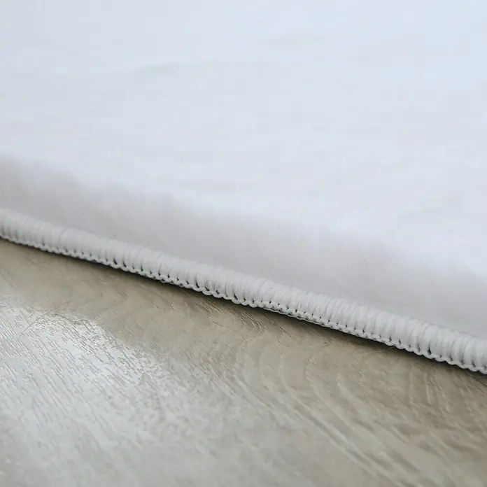 Hochflorteppich Pouffy - Weiß, 250 x 80 cm, 100 % Polyester - Detailaufnahme eines weißen Teppichs mit sauberer Kante auf einem hellen Holzboden, ideal für minimalistisches Design.