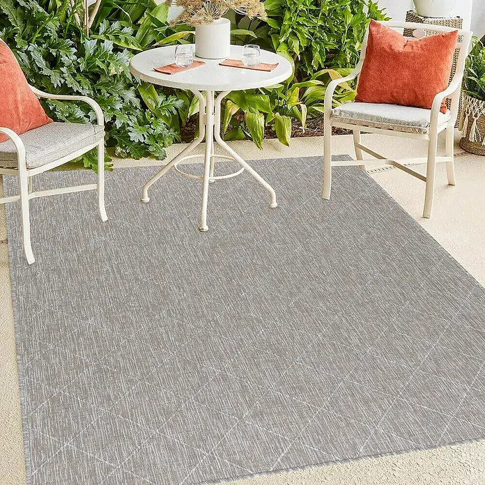 Outdoor-Teppich Zagora II - Beige, 170 x 120 cm, 100 % Polypropylen - Ein grauer Teppich mit geometrischem Muster liegt auf einer Terrasse mit Gartenmöbeln. Der Teppich sorgt für ein gemütliches Ambiente im Außenbereich.