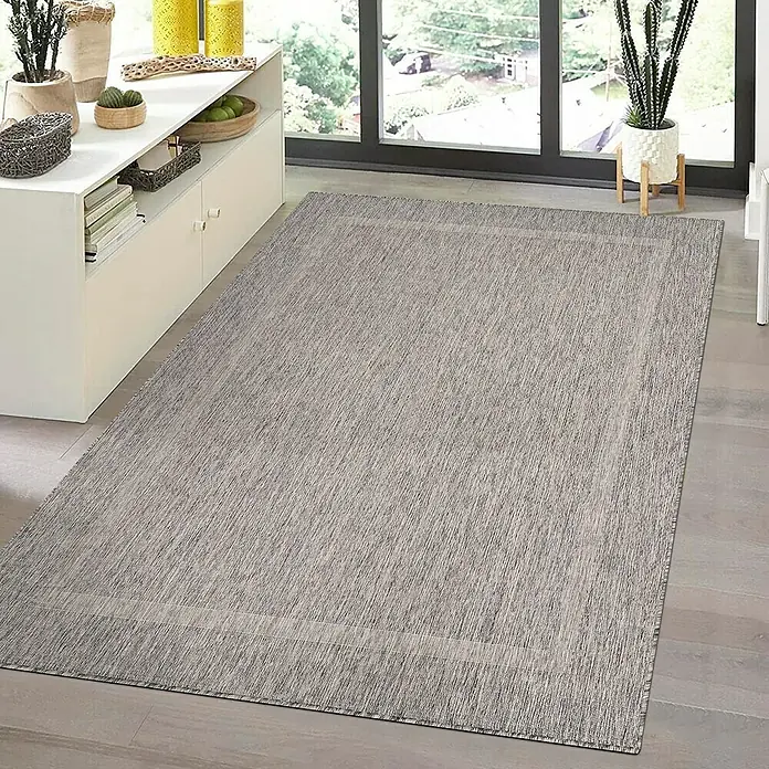 Outdoor-Teppich Relax - Grau, 200 x 140 cm, 100 % Polypropylen - Ein grauer Teppich mit rechteckigem Muster liegt auf einem Holzboden neben einem weißen Schrank und einem Fenster. Der Teppich verleiht dem Raum Wärme.
