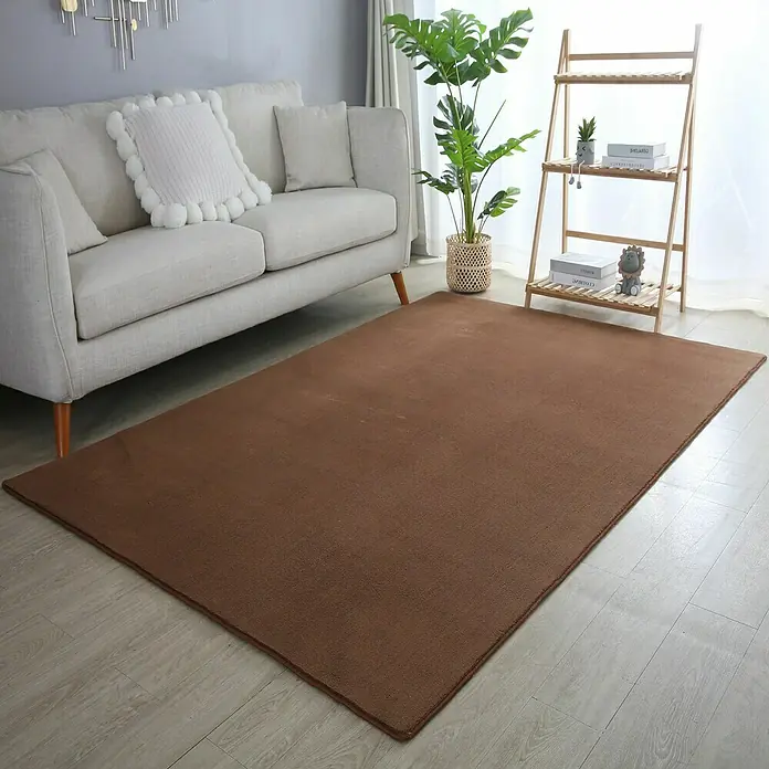 Kurzflorteppich Sky - Braun, 200 x 140 cm, 100 % Polyester - Ein satter, brauner Teppich liegt vor einem Sofa und schafft einen gemütlichen Raum mit seiner weichen Textur und warmen Farbe.