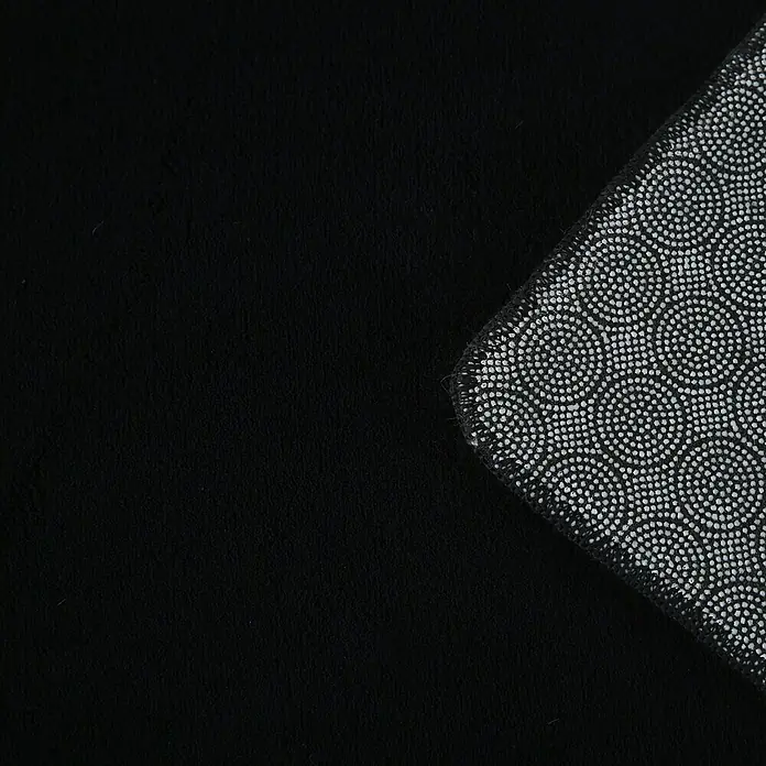 Kurzflorteppich Sky - Schwarz, 230 x 160 cm, 100 % Polyester - Detailaufnahme einer schwarzen Fußmatte mit rutschfester Unterseite. Die Matte bietet Komfort und Sicherheit auf glatten Böden.