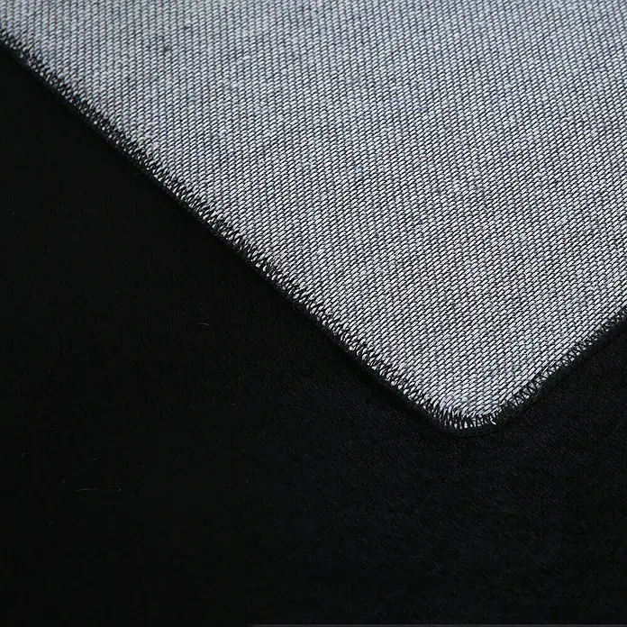 Hochflorteppich Pouffy - Schwarz, 150 x 80 cm, 100 % Polyester - Nahaufnahme einer grauen, fein gewebten Textur mit sauber vernähtem Rand auf einem schwarzen Hintergrund, ideal für Textil- oder Designprojekte.