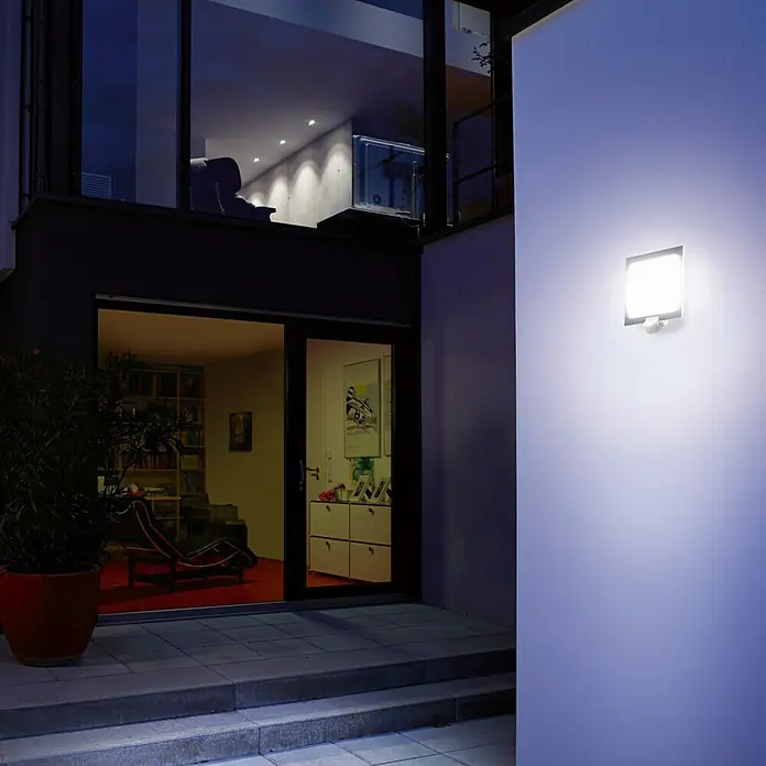 Steinel Sensor-Außenleuchte L 20 S anthrazit - 60 W, 8 x 24 x 23 cm, Anthrazit/Weiß, IP44 - Ein Außenwandleuchte beleuchtet einen modernen Hauseingang bei Nacht.