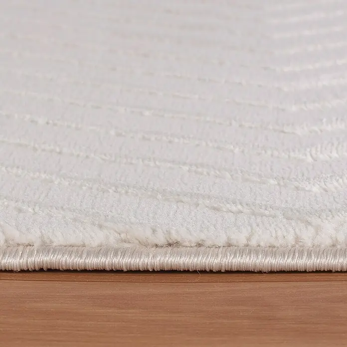 Kurzflorteppich Sahara IV - Creme, 230 x 160 cm, 100 % Polypropylen - Nahaufnahme eines weißen Teppichs mit sanften Rillen auf einem hellbraunen Holzboden, der eine weiche Textur und ein elegantes Design zeigt.