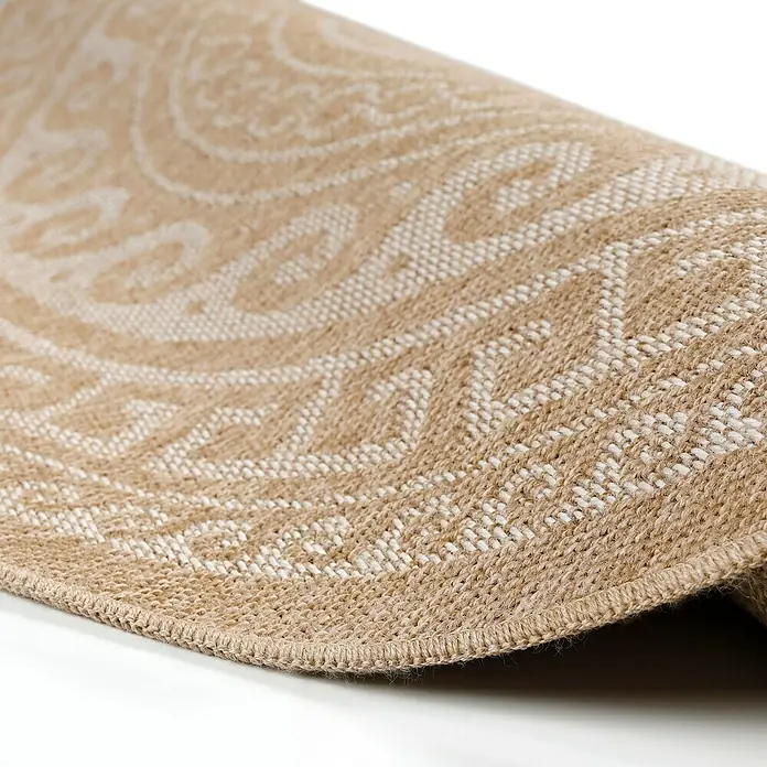 Outdoor-Teppich Comilla II - Beige, Durchmesser: 160 cm, 100 % Polypropylen - Nahaufnahme eines runden Teppichs mit hellbeigem Muster, der sich teilweise aufrollt und die Textur und Webart betont.