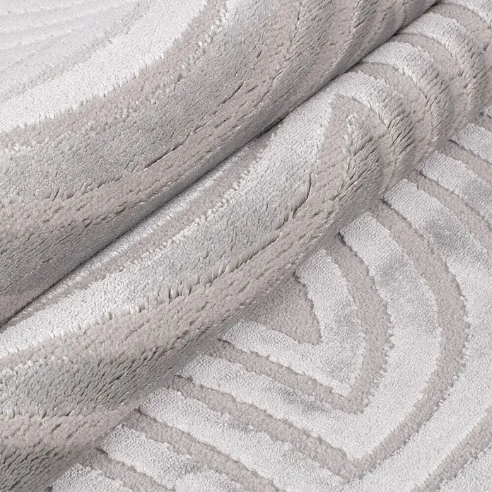 Kurzflorteppich Sahara II - Silber, 170 x 120 cm, 100 % Polypropylen - Nahaufnahme eines gerollten, weichen Teppichs mit einem modernen, geometrischen Muster in sanften Grautönen.