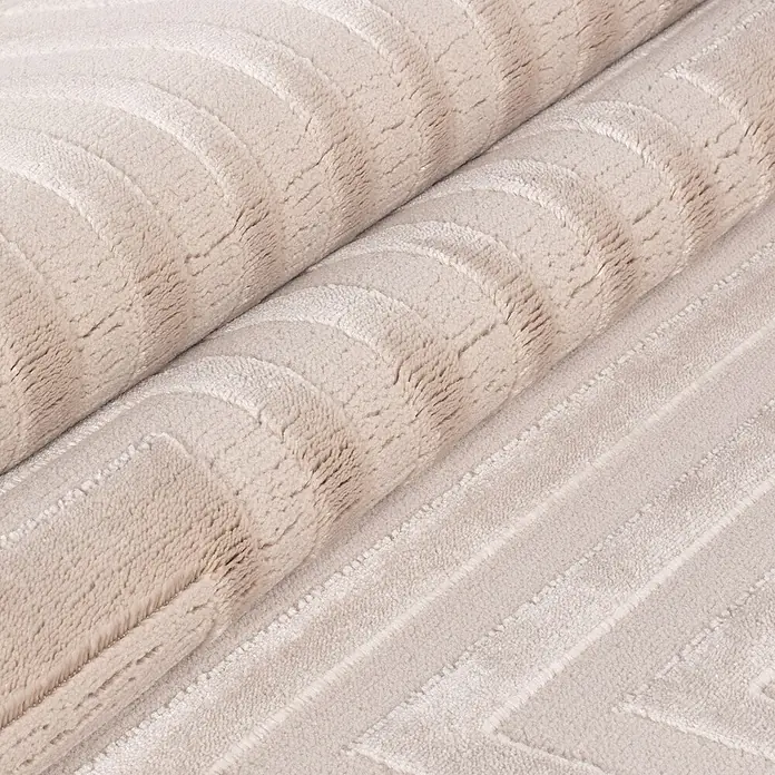 Kurzflorteppich Sahara V - Beige, 170 x 120 cm, 100 % Polypropylen - Nahaufnahme einer gerollten, beigen Badematte mit einem erhabenen, geometrischen Muster, das Textur und Komfort hervorhebt.