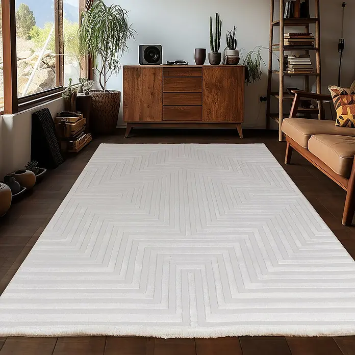 Kurzflorteppich Sahara V - Creme, 200 x 140 cm, 100 % Polypropylen - Ein weisser Teppich mit geometrischem Muster liegt in einem stilvollen Wohnzimmer mit Holzmöbeln und Zimmerpflanzen.