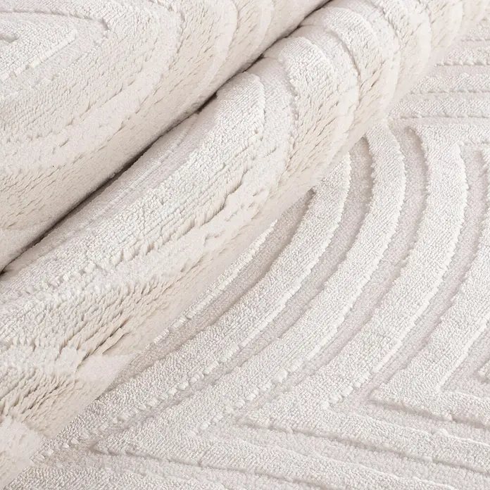 Kurzflorteppich Sahara II - Creme, 200 x 140 cm, 100 % Polypropylen - Detailaufnahme eines gerollten, elfenbeinfarbenen Teppichs mit einem erhabenen, geometrischen Muster, das Textur und Design hervorhebt.